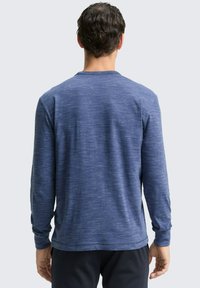 Langärmliges Hemd aus meliertem marineblauen Stoff, weicher Textur, Rundhalsausschnitt und tailliertem Design mit sanft zulaufenden Ärmeln.