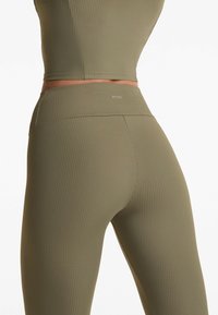 Set de activewear cu dungi de culoare verde măsliniu, format dintr-un top ajustat și colanți cu talie înaltă, având un detaliu cu logo pe banda de la talie.