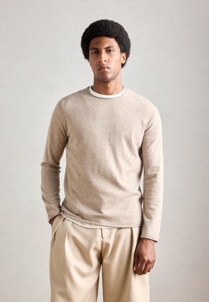 Beige long-sleeve sweater with a subtle texture, featuring a white collar trim. Paired with light beige pleated trousers.