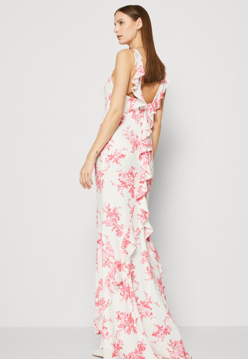 Femme se tenant de profil, portant une robe sans manches blanche à fleurs avec des fleurs roses et des volants dans le dos et sur le côté.