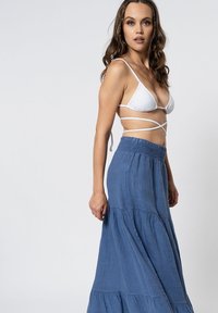 Gonna maxi in lino blu con un design a strati, dotata di una vita elasticizzata, abbinata a un top bikini bianco a triangolo.