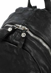 Zaino in pelle nera con compartimenti zip, hardware in argento e una finitura liscia leggermente strutturata. Primo piano dei dettagli di design.