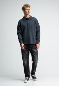 Dunkelblaues, strukturiertes Langarmpoloshirt mit Kragen und drei Knöpfen, kombiniert mit ausgewaschenen schwarzen Jeans und schwarzen Sneakers.