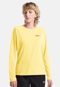 Langärmliges, gelbes technisches Shirt mit Rundhalsausschnitt und Logo-Akzenten auf der Brust. Glatte Textur und leichtes Material.