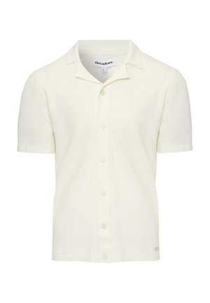 Chemise à manches courtes, col rabattu en tissu texturé blanc cassé, avec un bouton sur le devant et une étiquette de marque discrète à l'ourlet.