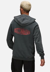Felpa con cappuccio in carbone, con una grande grafica sbiadita rossa "BUCCANEERS" sul retro; presenta una tasca a marsupio frontale e un cappuccio regolabile.