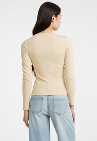Top beige a maniche lunghe con un design aderente, texture a coste e scollatura rotonda, abbinato a jeans azzurri a gamba larga con tasche posteriori.