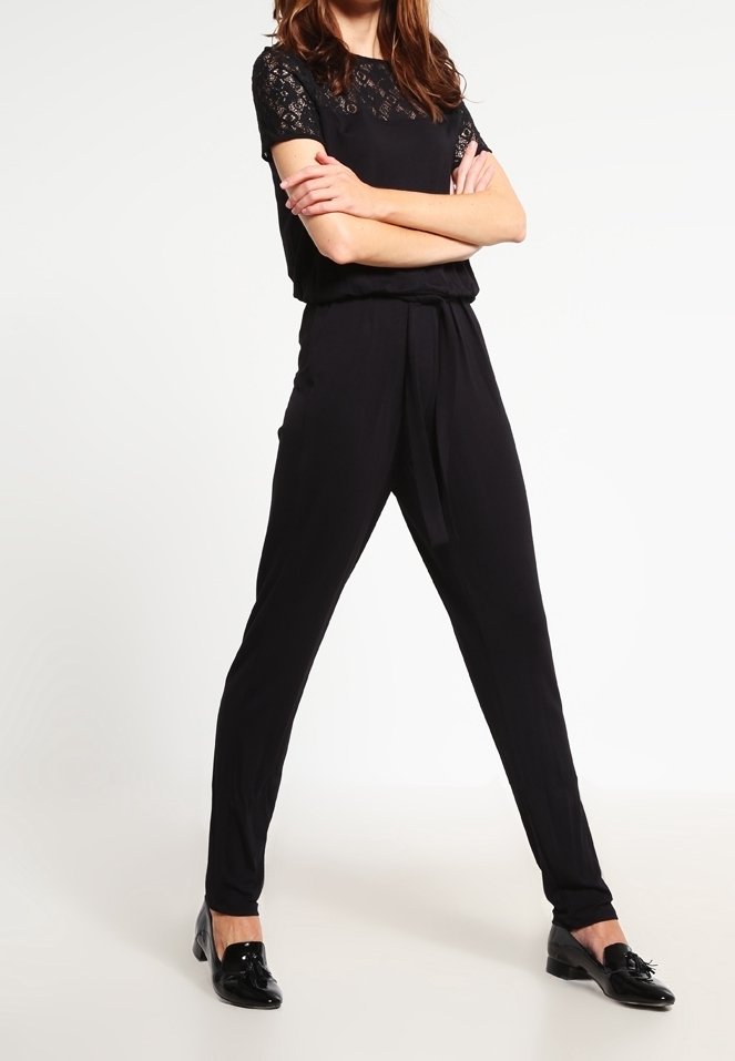 Černý overal s krajkovými krátkými rukávy, elastickým pasem, zúženými nohavicemi a hladkou texturou látky, doplněný o černé balerínky.