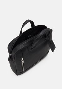 Sac à main en cuir noir avec une finition texturée, double anses supérieures, quincaillerie en argent et une poche zippée à l'avant. L'intérieur présente un motif de logo.