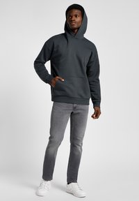 Dark gray hooded sweatshirt with a front pocket, paired with light gray jeans and white sneakers. Simple, casual design with a soft texture.