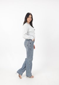 Grå stickad cardigan med knäppning fram, tillsammans med ljusblå högmidjade utsvängda jeans. Sandaler med genomskinlig rem och öppen tå.