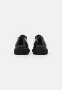 Sorte lakkleder sko med en glatt, skinnende overflate, avrundede bakskudd og en tykk, strukturert svart såle. Rent design med minimale detaljer.