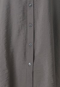 Camisa cinza de botão, feita de um tecido leve e texturizado, com uma fila de botões metálicos na frente e um corte descontraído.