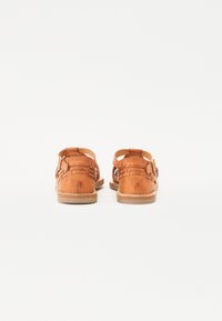 Brune skinnsandaler med vevd design, åpen bak og spennefeste. Sålen er lys brun med sømdetaljer langs kanten.