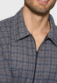 Giacca grigia con zip, caratterizzata da un motivo a scacchi e una texture morbida. Presenta un colletto e una zip a contrasto, adatta per un abbigliamento informale.