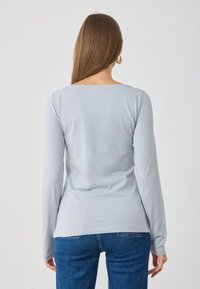 Maglietta azzurra chiara a maniche lunghe con scollatura rotonda e vestibilità aderente, realizzata in tessuto morbido e elasticizzato. Design minimalista, senza motivi o decorazioni.