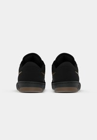Zapatillas negras con una parte superior texturizada, que cuentan con una suela negra plana y una suela exterior de goma marrón. Diseño minimalista y sin patrones visibles.