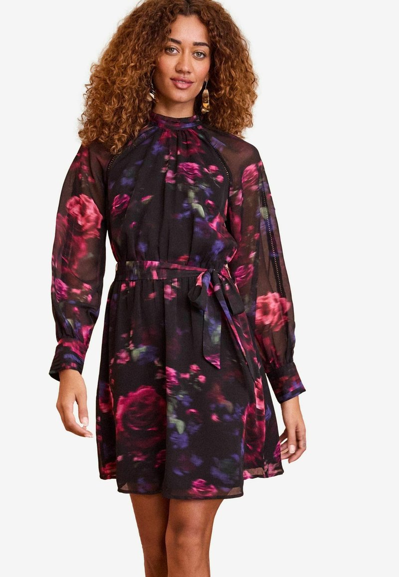 Melna ziedu kleita ar augstu apkakli, caurredzamu garo piedurkņu, elastīgu jostasvietu un sasaistes jostu. Iekļauj rozā un purpura rozes ziedu rakstus.