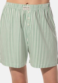 Groene en witte gestreepte boxers gemaakt van zachte stof, met een knoopsluiting aan de voorkant en een elastische tailleband met een klein label.