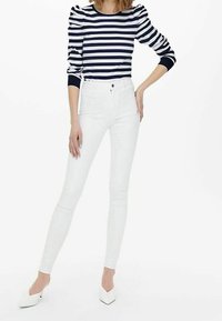 Maglietta a righe blu navy e bianca con maniche a sbuffo, abbinata a jeans skinny bianchi e tacchi a punta bianchi. Tessuto liscio e design aderente.