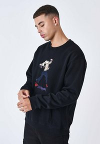 Sweatshirt noir, en mélange de coton, avec un motif brodé d'un personnage en jeans bleus et chaussures rouges, avec des poignets et un col côtelés.