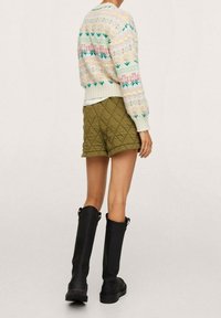 Pull multicolore en tricot avec motifs floraux, shorts matelassés vert olive et bottes noires montantes jusqu'au genou, vus de dos.