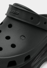 Prim-plan al unei papuci Croscs negre, arătând orificiile de ventilație, talpa texturată și cureaua de călcâi cu numele mărcii.