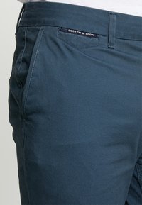 Granatowe chinosy z bawełny z usztywnionym paskiem, kieszeniami bocznymi oraz metką z logo "Scotch & Soda" w pobliżu talii.