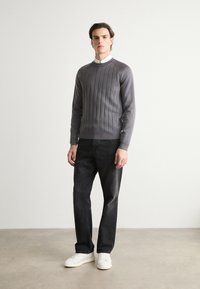 Grau gestreifter Pullover mit rundem Ausschnitt, kombiniert mit dunklen Jeans und weißen Sneakers. Einfaches Design mit einem strukturierten Muster auf dem Pullover.