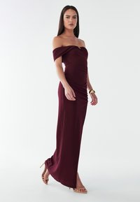 Burgundia õlast vabalt langev kleit, volditud detailidega, kitsas lõige, põrandapikkune disain ja pehme, sile materjal. Rikkaid aktsente annavad peened metallosad.