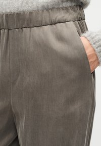 Gray fabric trousers with a smooth texture, elastic waist, side pocket, and subtle vertical pattern, partially tucked under a light sweater.