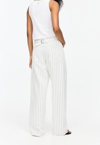 Pantalon large blanc à rayures avec un détail ceinture, deux poches arrière et une texture lisse, associé à un haut blanc sans manches.