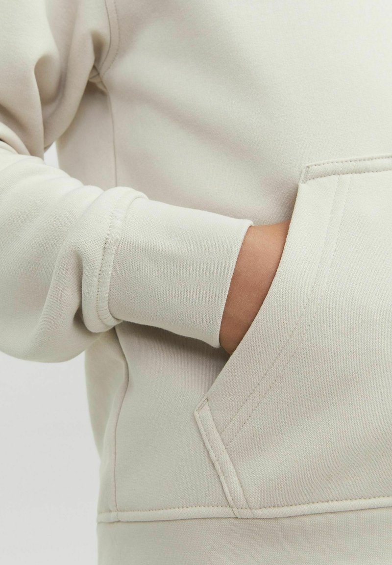 Sweatshirt beige clair avec une poche kangourou, des poignets côtelés et un tissu en coton lisse au toucher doux.