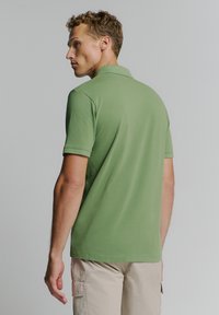 Groene poloshirt van zachte stof, met een kraag en korte mouwen. De achterkant is eenvoudig en heeft een losse pasvorm, wat goed past bij beige shorts.