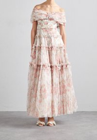 Axelklänning i blommönster i genomsiktig tyg, med lager av volanger, fransade kanter och mjuka rosa och krämfärgade nyanser. Bärs med lätta sandaler.