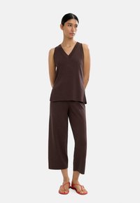 Brązowy top bez rękawów z dekoltem w kształcie litery V, zestawiony z szerokimi brązowymi spodniami. Podkreślony czerwonymi płaskimi sandałami. Gładki materiał, luźny fason.