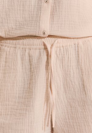 Pantalon en tissu beige doux et texturé avec taille élastique et cordon noué, associé à un haut boutonné assorti.