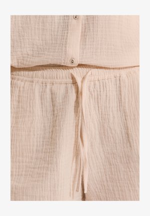 Pantalon en tissu beige doux et texturé avec taille élastique et cordon noué, associé à un haut boutonné assorti.