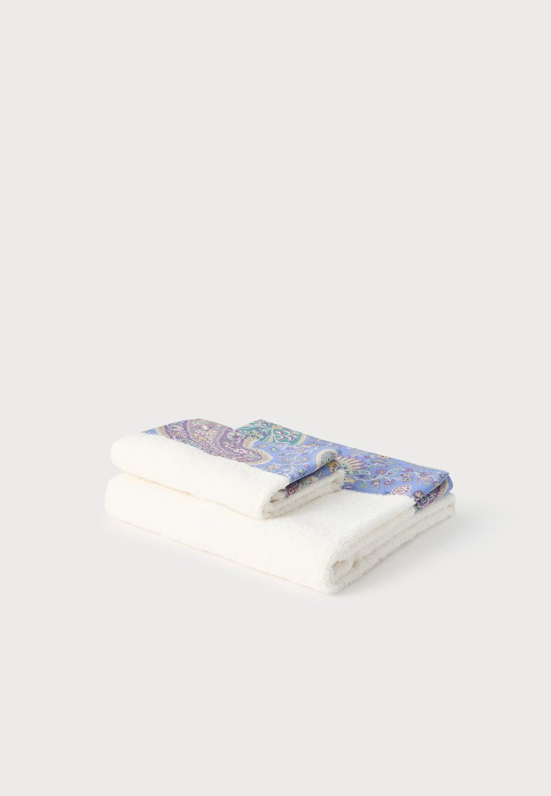 Deux serviettes blanches pliées avec des bordures à motifs paisley bleus et violets sur un fond uni gris clair.