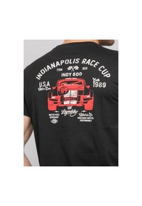 T-shirt noir à manches courtes présentant un graphique rouge d'une voiture de course vintage avec un texte blanc, comprenant "Indianapolis Race Cup" et "1989."