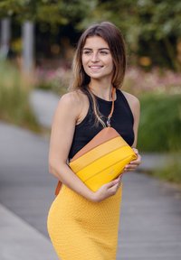 Žlutá a hnědá křížová taška s horizontálními pruhy, hladká kožená textura, s malým logem a nastavitelným popruhem.