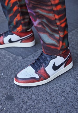 Chaussures avec des baskets Nike rouges, blanches et noires associées à un pantalon multicolore orange et violet à motifs sur un revêtement en asphalte.