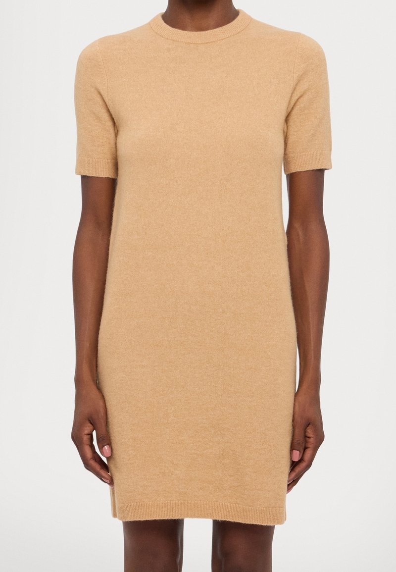 Robe ajustée à manches courtes, de couleur beige clair, réalisée en maille douce. Elle présente un col rond ainsi que des poignets et un ourlet côtelés.