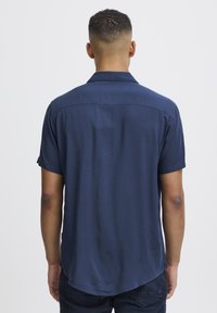 Camicetta a maniche corte di colore blu navy realizzata in tessuto liscio, con un colletto semplice, cuciture sulla spalla posteriore e un design con orlo curvo.