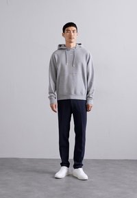 Sweat à capuche gris avec une poche kangourou, associé à un pantalon tailleur bleu marine et des baskets blanches. Texture lisse et coupe décontractée.