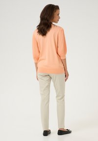Pull over couleur pêche avec des manches côtelées, associé à un pantalon beige clair et des ballerines noires, offrant une coupe décontractée.