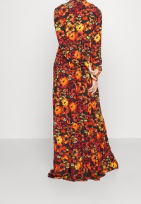 Dlouhé květinové šaty v černé barvě s živými oranžovými a žlutými květy. Mají dlouhé rukávy a lehkou siluetu s volány.