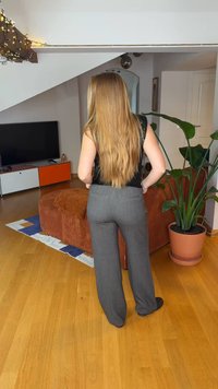 Γκρι, ραμμένο κοστούμι με ίσια γραμμή παντελονιού, με πίσω τσέπες. Το περιβάλλον περιλαμβάνει καφέ καναπέ και πράσινο φυτό.