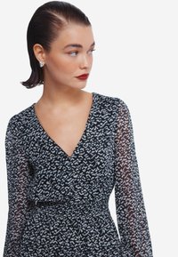 Mustapitsinäinen kietaisumekko, jossa on pitkät läpikuultavat hihat ja V-pääntie, ja joka sisältää solmittavan vyön korostamaan vartalonmuotoa.