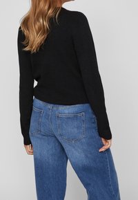 Pull tricoté noir à manches longues, associé à un jean bleu clair taille haute avec deux poches arrière et une coupe légèrement ample.
